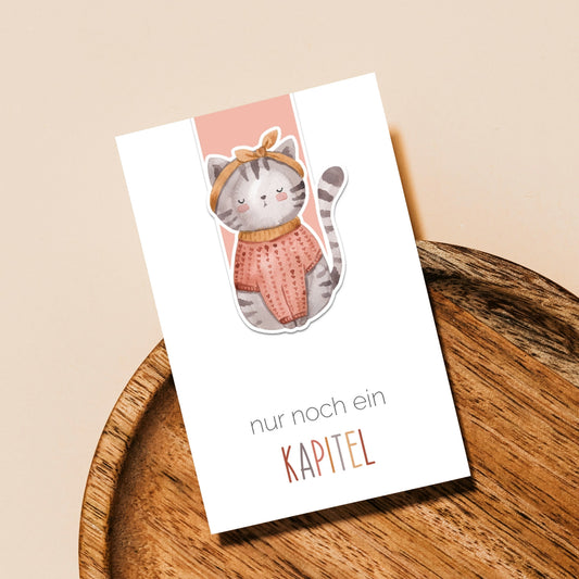 Magnetisches Lesezeichen Katze auf einem Holztablett, zeigt eine Katze in Pullover und Schleife, ideal für Buchliebhaber und handgemacht auf hochwertigem Papier.