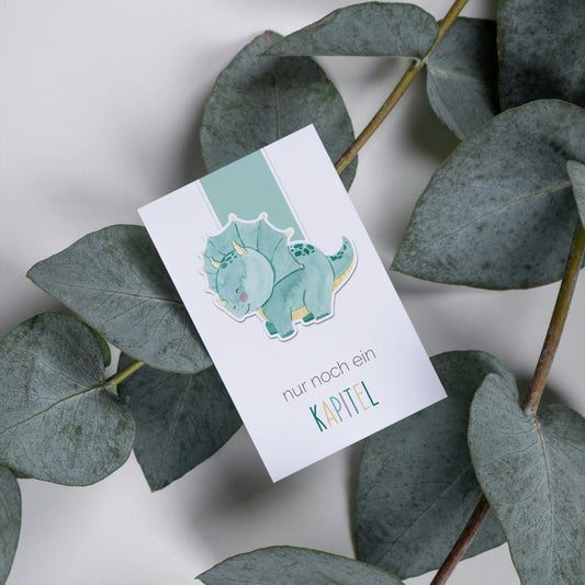 Magnetisches Lesezeichen Dino zeigt handgemalten Dinosaurier auf Karte, umgeben von Eukalyptus. Ideal für Buchliebhaber, aus robustem, versiegeltem Papier.