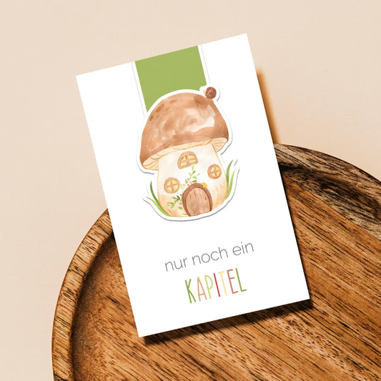 Magnetisches Lesezeichen Pilzhaus auf Holztablett, zeigt handgemaltes Pilzhausmotiv, ideal für Buchliebhaberinnen. Hergestellt aus hochwertigem Papier, ca. 6 x 3,5 cm.