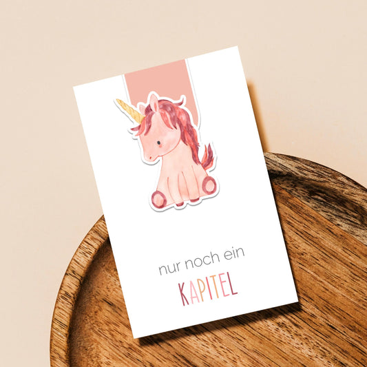 Magnetisches Lesezeichen Einhorn: Handgemaltes Einhorn-Design, ca. 6 x 3,5 cm, aus 200g Papier mit Vinyl versiegelt, enthält Magnete für sicheren Halt. Auf Tablett präsentiert.