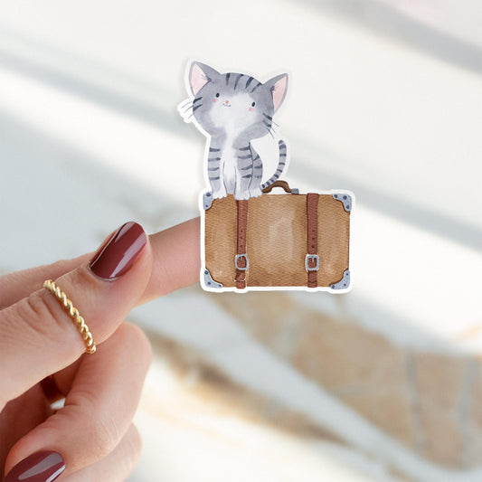 Sticker Katze & Koffer: Hand hält handgemalten Katzen-Sticker auf einem Koffer. Hochwertiger, spritzfester Vinyl-Aufkleber, ideal für Reisen und Dekoration.