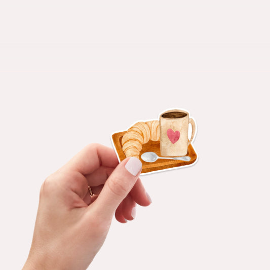Sticker Frühstück: Hand hält Vinyl-Aufkleber mit Kaffee- und Croissant-Motiv, ideal für Bullet Journals, Laptops oder Einladungen. Spritzfest, langlebig und handgefertigt.