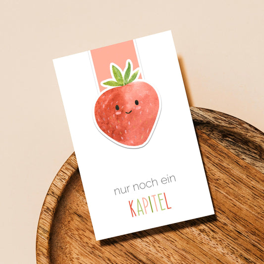 Magnetisches Lesezeichen Erdbeere auf Holztablett, zeigt eine lächelnde Erdbeere mit Text nur noch ein KAPITEL. Ideal für Buchliebhaber, handgemacht, robust und langlebig.