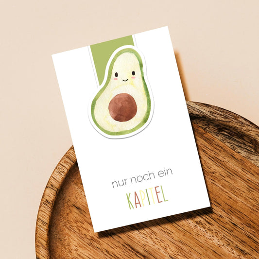 Magnetisches Lesezeichen Avocado in einem Holzschale, zeigt lachende Avocado-Illustration und den Text „nur noch ein KAPITEL“, mit grünem Tab oben.