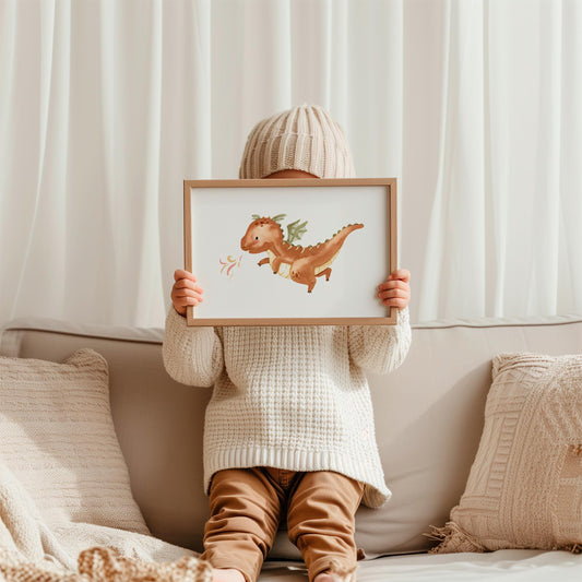 Kind hält gerahmtes Poster Feuerdrache A3 & A4 mit braunem Drachen, grünen Flügeln, gemalt in Aquarellstil, auf einer Couch sitzend, hoch.
