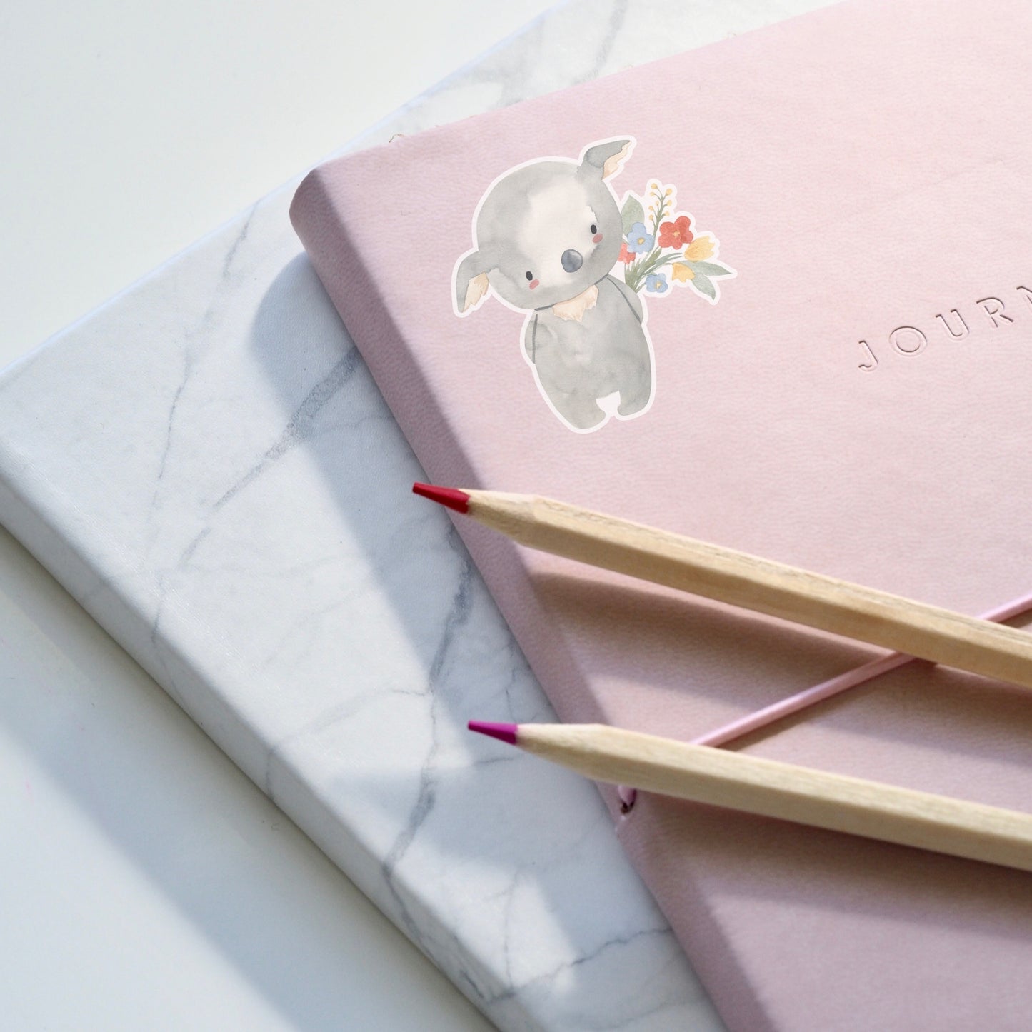 Sticker Koala & Blumen: Pinkes Notizbuch mit Cartoon-Koala, der Blumen hält, und zwei Bleistiften. Hochwertiger, langlebiger Vinyl-Sticker für individuelle Gestaltung.