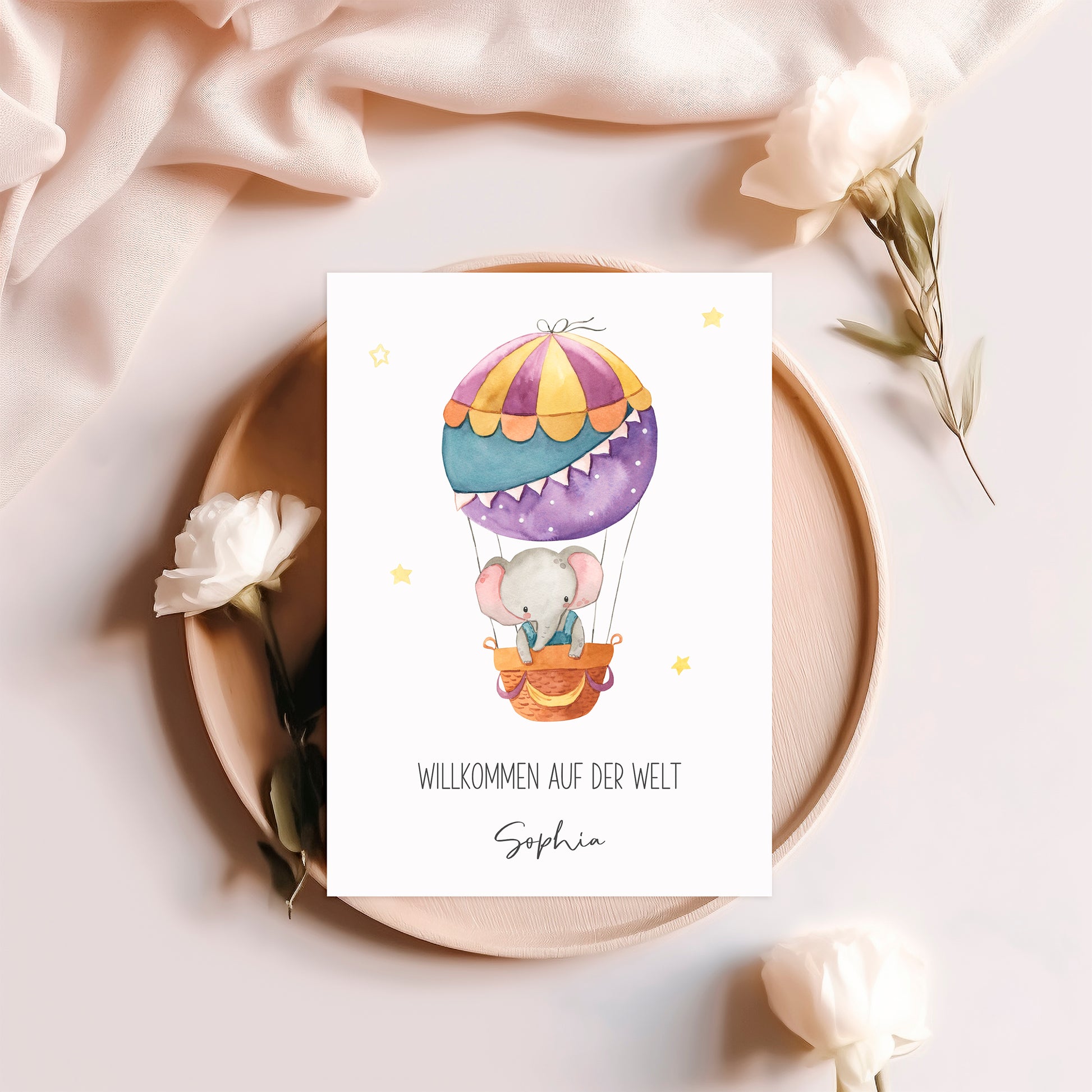 Personalisierte Geburtskarte Elefant & Heißluftballon A6 auf Holzplatte mit Blumen, zeigt Elefant im Ballon, Willkommen auf der Welt und Name Sophia.