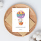 Personalisierte Geburtskarte Elefant & Heißluftballon A6, zeigt Aquarell eines Elefanten im Ballon mit „Willkommen auf der Welt, Felix“, auf rundem Holztablett.