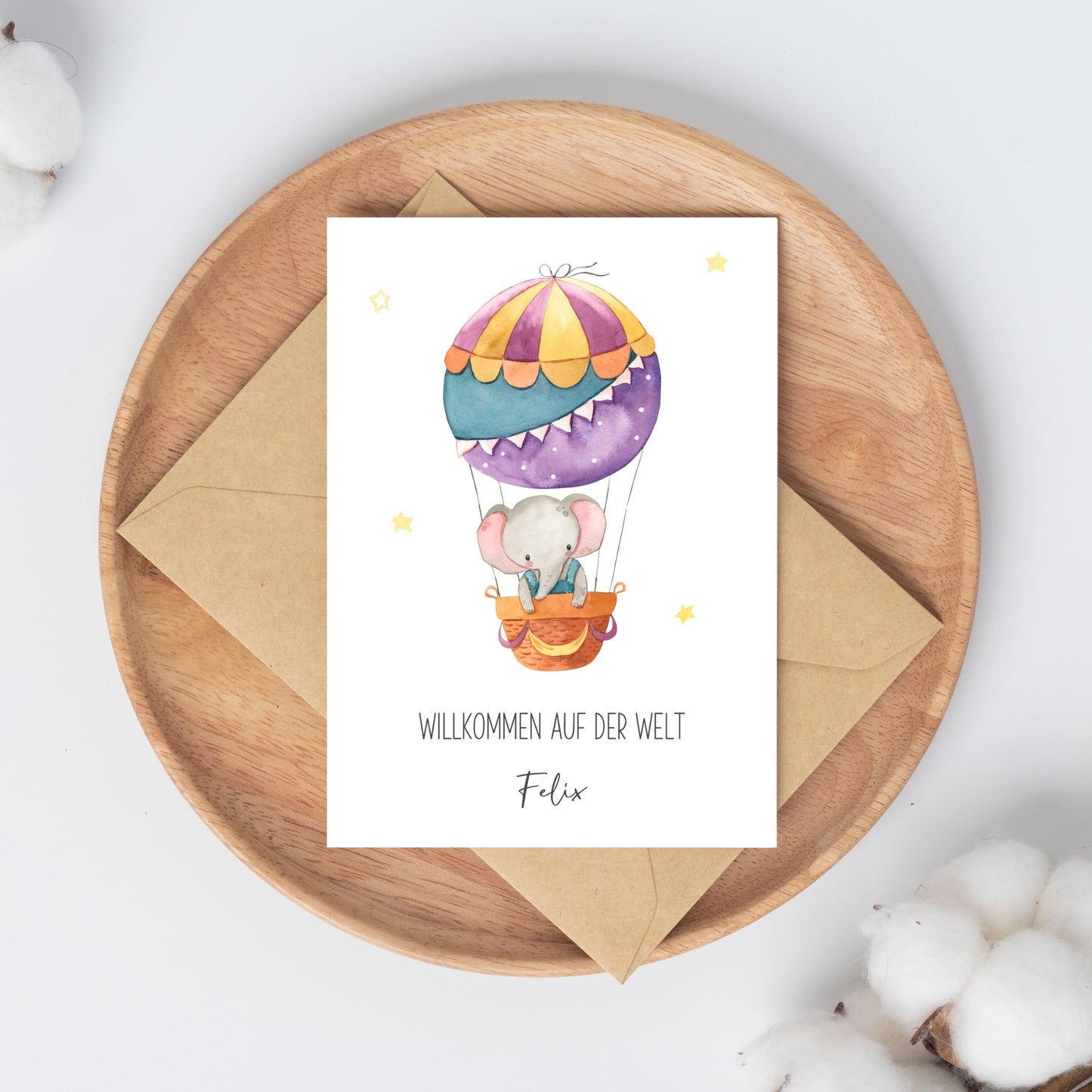 Personalisierte Geburtskarte Elefant & Heißluftballon A6, zeigt Aquarell eines Elefanten im Ballon mit „Willkommen auf der Welt, Felix“, auf rundem Holztablett.