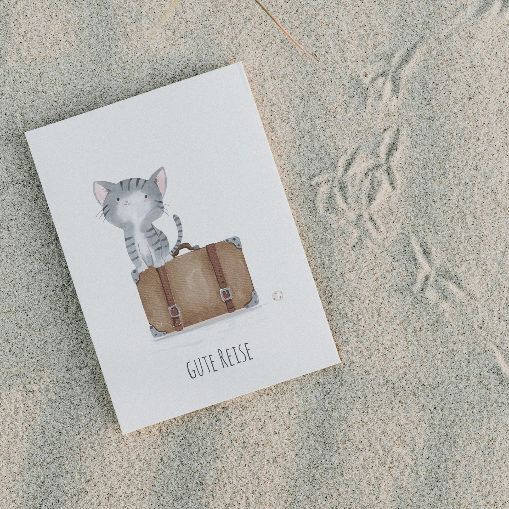 Postkarte Karte Gute Reise Katze A6: Katze auf einem Koffer sitzend, daneben ein Ball, Text: Gute Reise. Auf hochwertigem, mattem Naturpapier gedruckt.