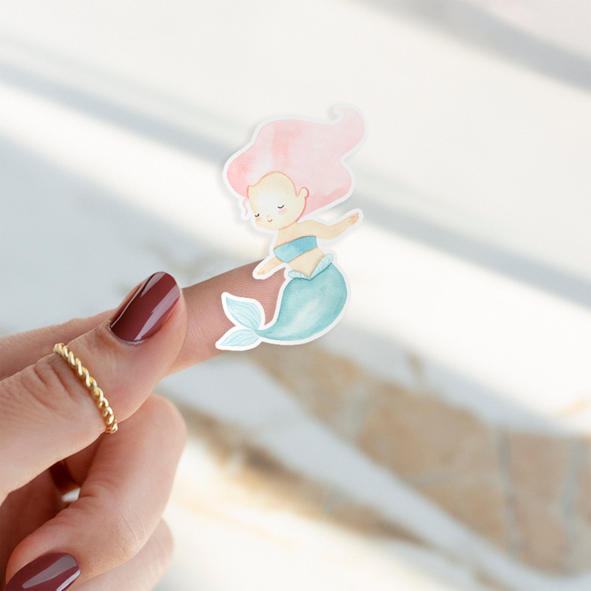 Finger mit einem Sticker Meerjungfrau pink, handgemalt in Pastelltönen, zeigt einen cartoonhaften Meerjungfrau-Aufkleber, ideal für Bullet Journals oder Handys.
