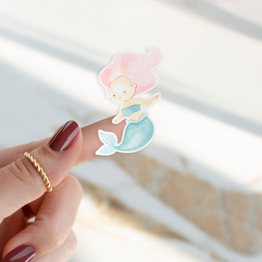 Finger mit einem Sticker Meerjungfrau pink, handgemalt in Pastelltönen, zeigt einen cartoonhaften Meerjungfrau-Aufkleber, ideal für Bullet Journals oder Handys.
