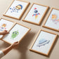 Posterset Astronauten A3 & A4: Sechs Holzrahmen mit Weltraum-Aquarellmotiven, darunter Astronauten-Tiere und UFO, an einer strukturierten Wand, geeignet für Kinderzimmer.