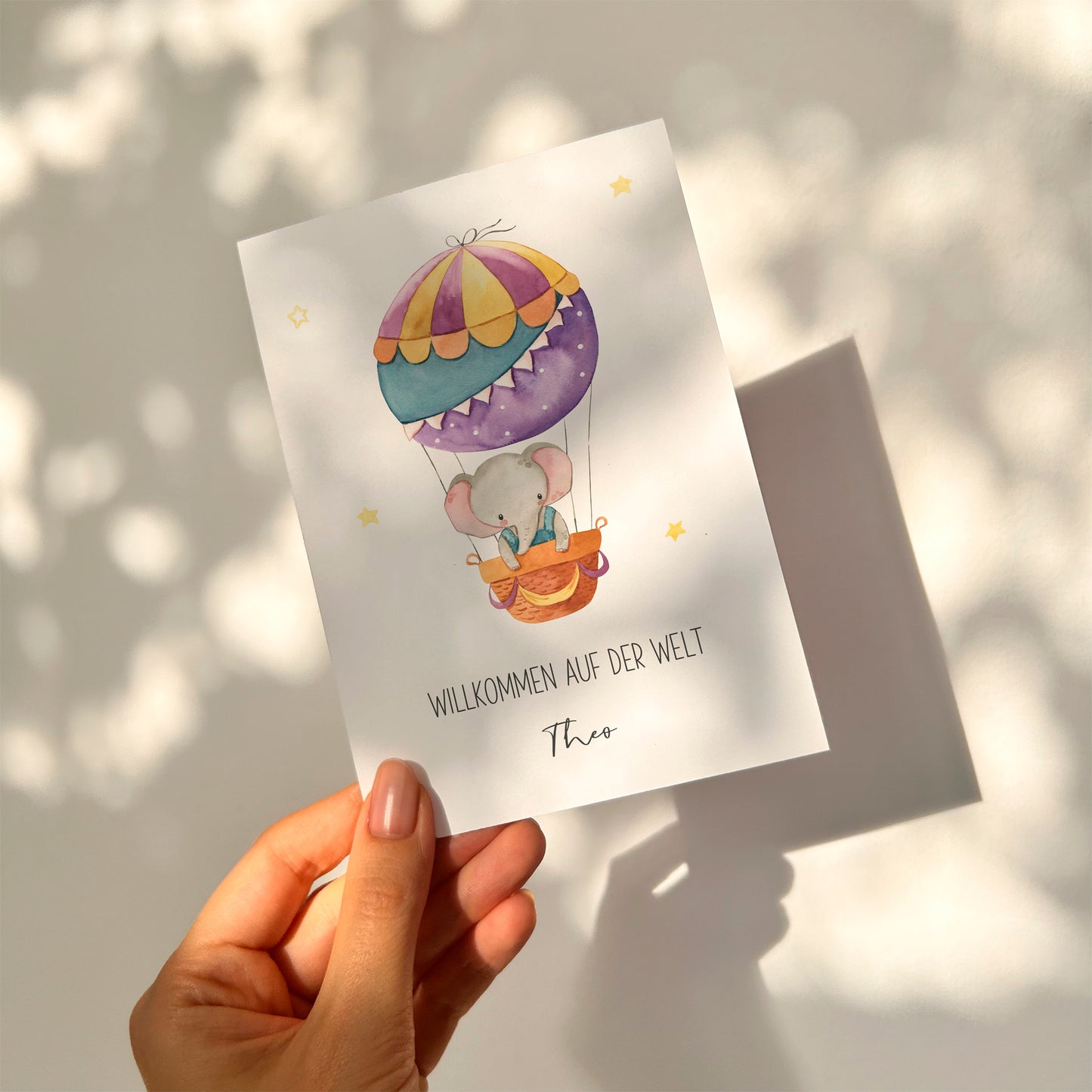 Personalisierte Geburtskarte Elefant & Heißluftballon A6 zeigt einen Elefanten im Heißluftballon mit „Willkommen auf der Welt“ und personalisiertem Namen „Theo“.