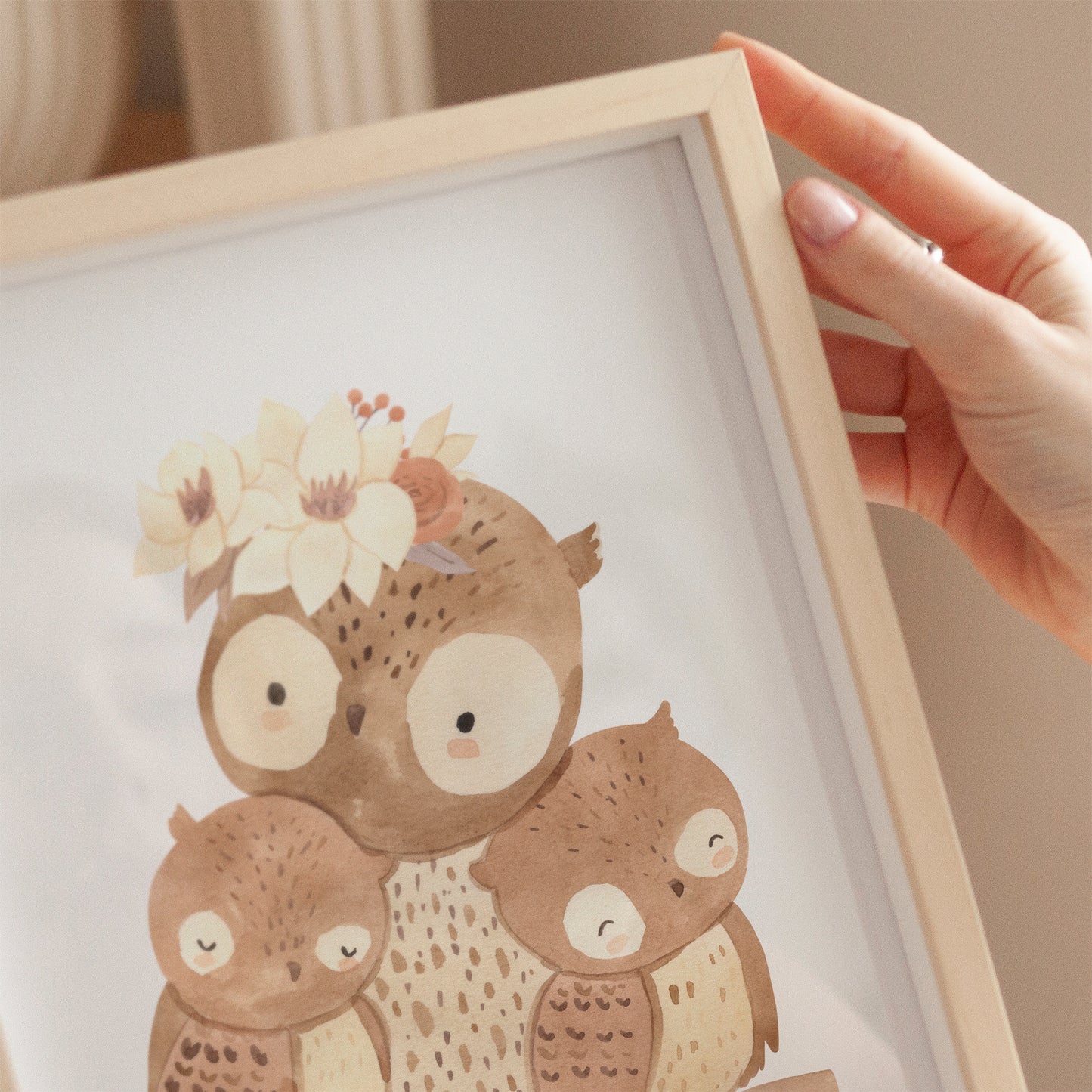Person hält Poster Mama Eule A4 & A3: Handgezeichnetes Poster mit einer Eulenmutter und ihren Babys auf einem Ast, mit Blumenkranz. Ideal für das Kinderzimmer.