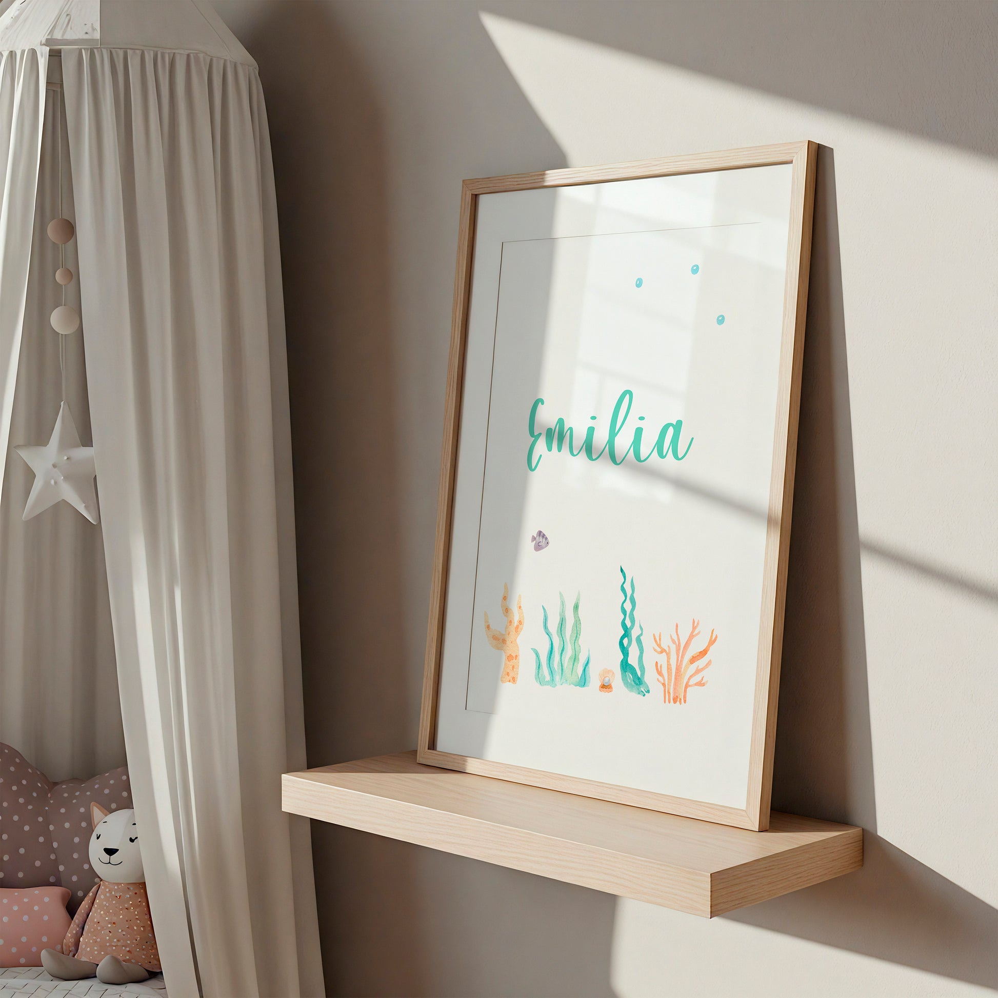 Personalisierter Namensposter-Teil eines 3er Sets: Meerjungfrau, A3 & A4, auf leichtem Regal im Kinderzimmer mit Emilia in grüner Kursivschrift und maritimen Motiven.