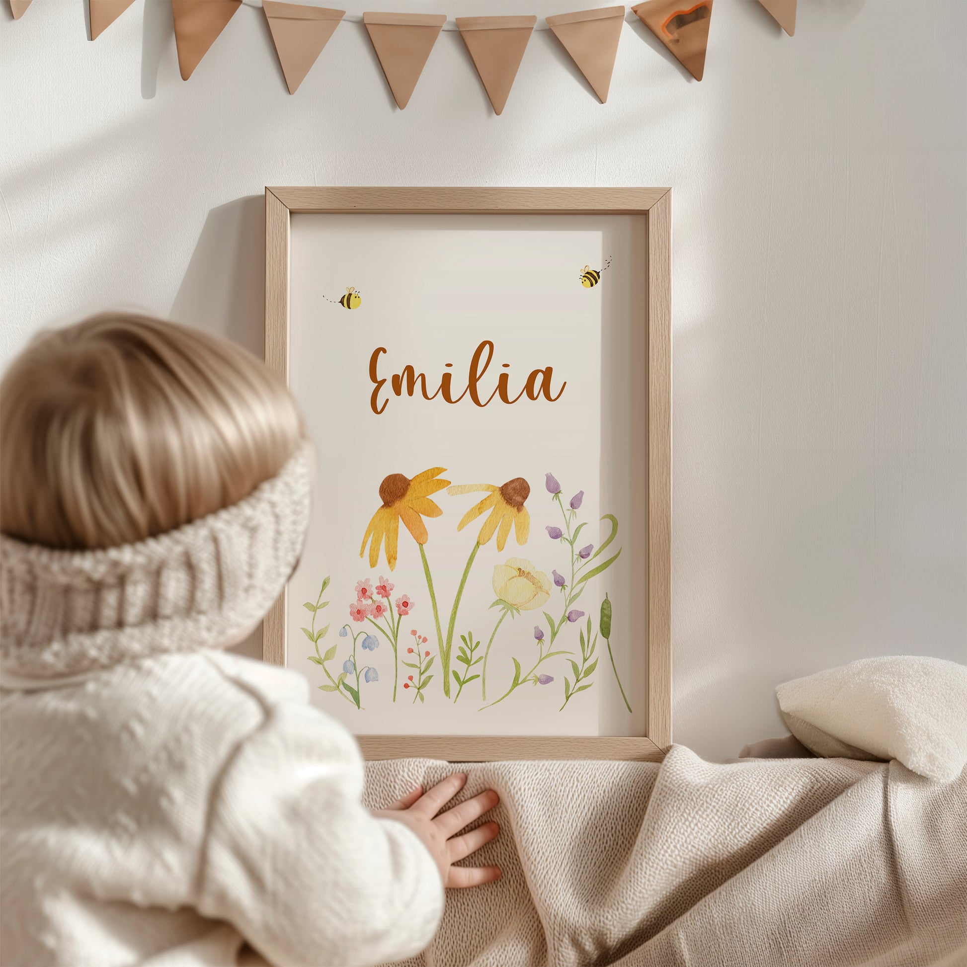 Kleinkind betrachtet personalisiertes Namensposter „Emilia“ mit Bienen und Blumen im Holzrahmen, Teil des 3er-Sets „Namensposter personalisiert im 3er Set: Bären und Bienen A3 & A4“.
