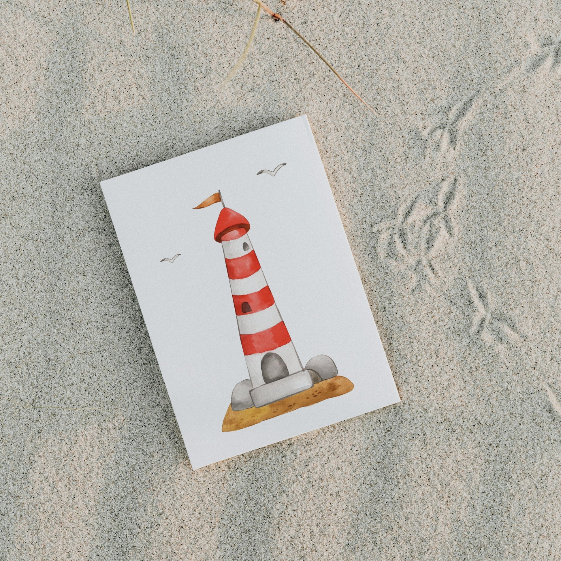 Postkarte Leuchtturm A6 auf Sand, zeigt einen rot-weiß gestreiften Leuchtturm mit Möwen. Gedruckt auf stabilem 300g Naturpapier, ideal für maritime Grüße.