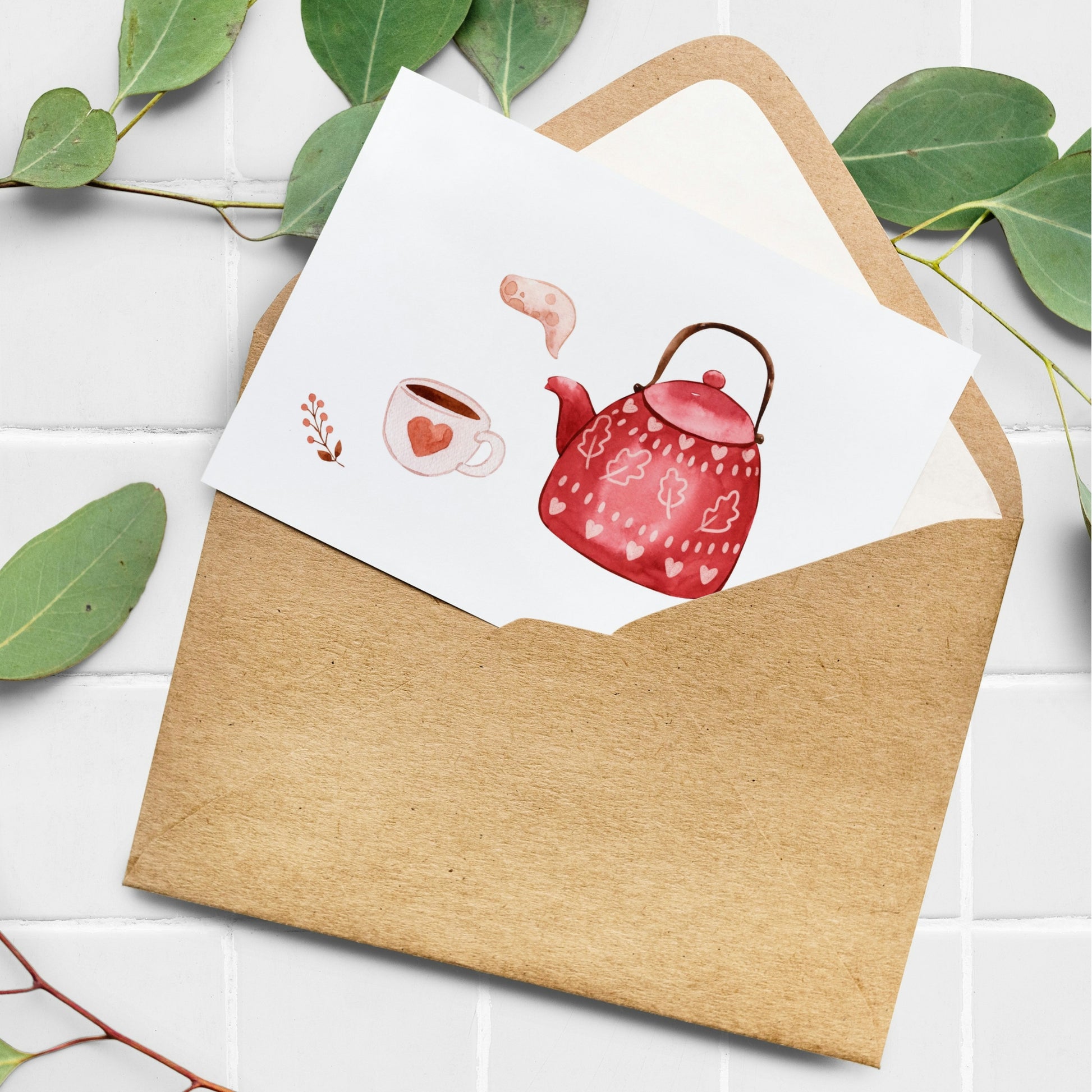 Karte Tea Time A6 mit Aquarell-Teekanne und Tasse, dekoriert mit Herzen und Blättern, in braunem Umschlag auf weißem Untergrund, umrahmt von Eukalyptus.
