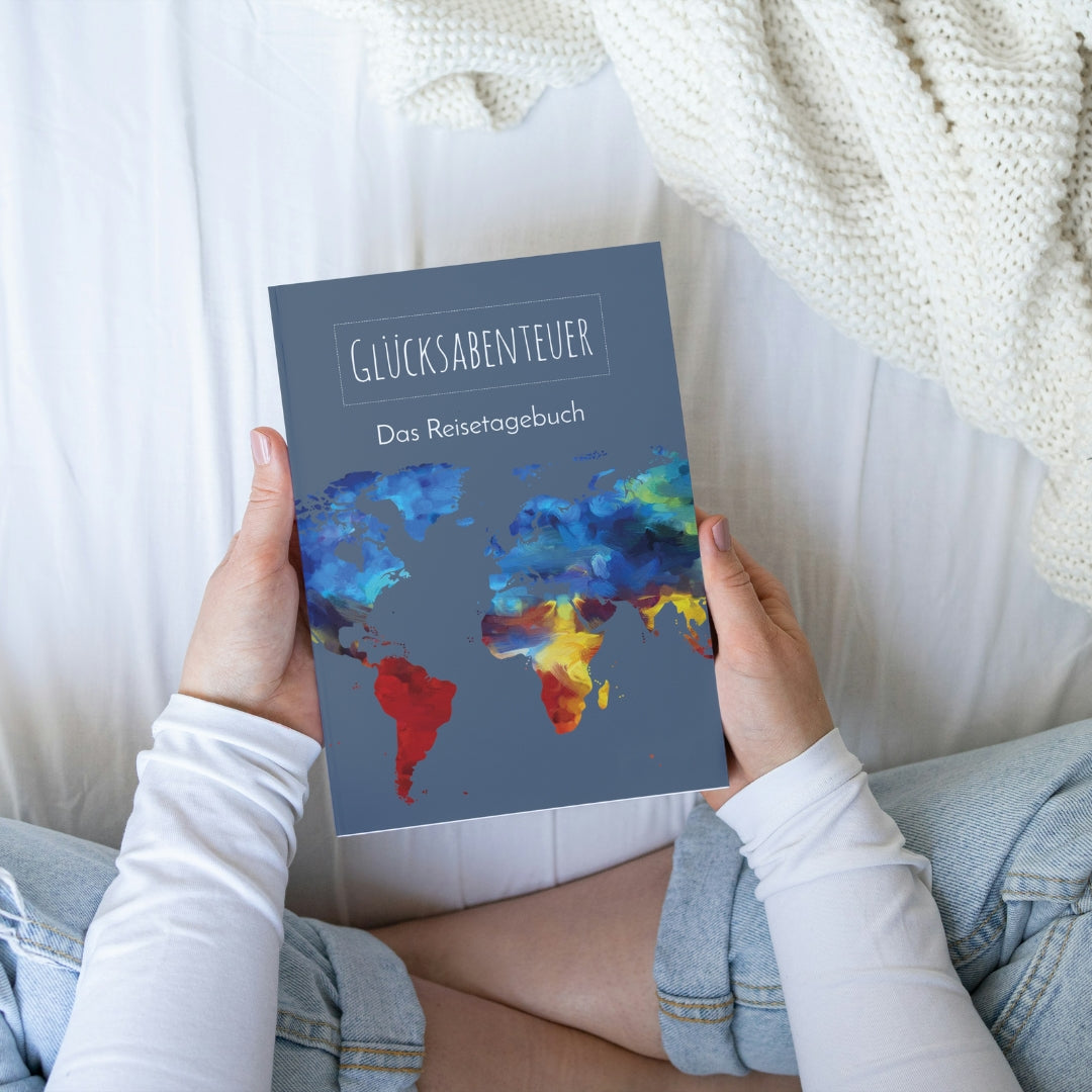 Person hält Reisetagebuch A5 Softcover mit bunter Weltkarte. Ideal zum Planen und Festhalten von Reiseerinnerungen.