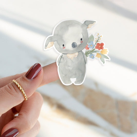 Sticker Koala & Blumen: Eine Hand hält einen Vinyl-Sticker eines handgemalten Koalas mit Blumen. Der Sticker ist spritzfest und ideal für kreative Verzierungen.