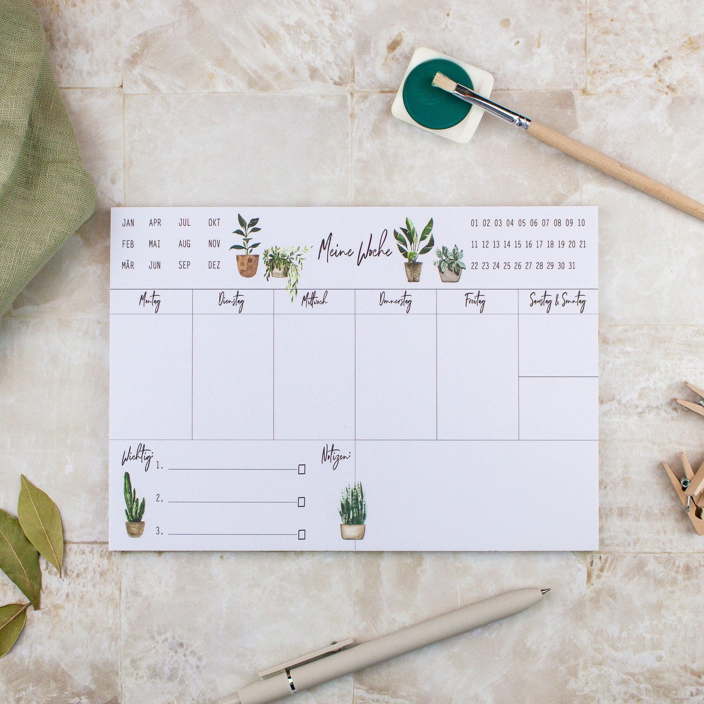 Wochenplaner Pflanzen A5 Block: Ein Wochenplaner mit handgemalten Pflanzenillustrationen, einem Stift und Pinsel auf Papier, perfekt für Termine, Notizen und To-dos.