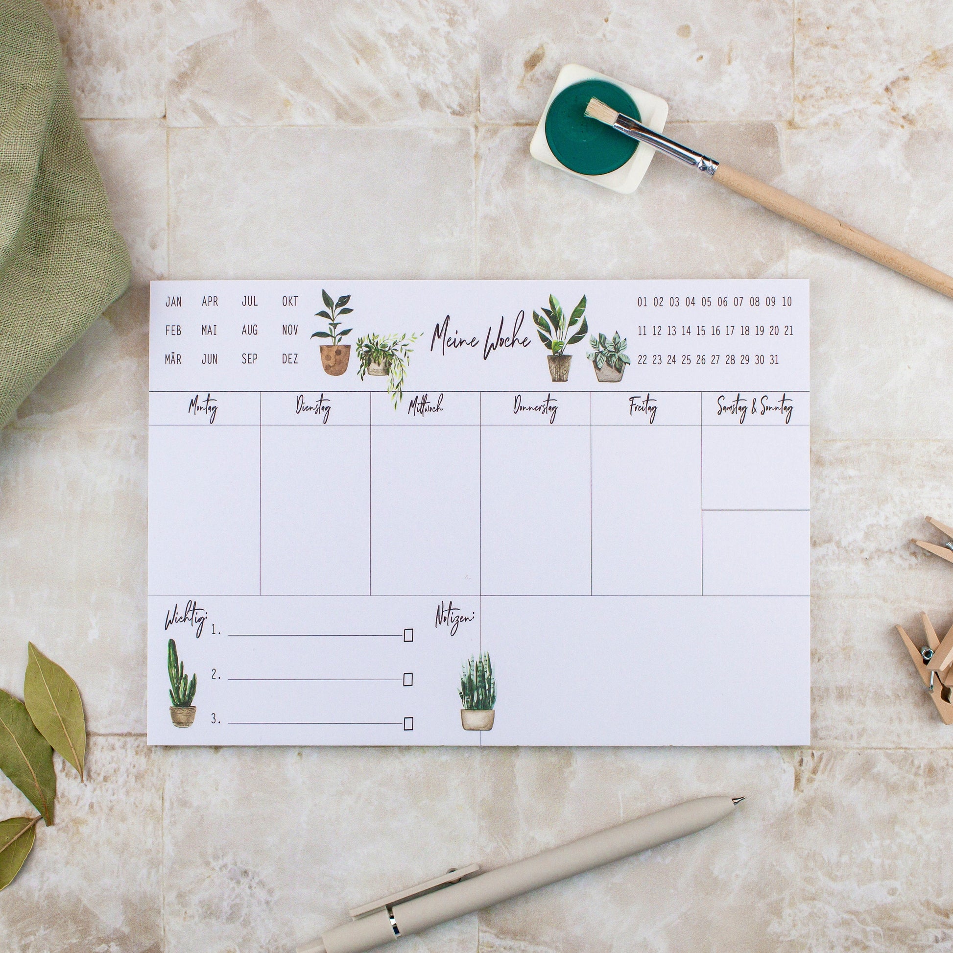 Wochenplaner Pflanzen A5 Block: Ein Wochenplaner mit handgemalten Pflanzenillustrationen, einem Stift und Pinsel auf Papier, perfekt für Termine, Notizen und To-dos.