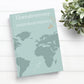 Reisetagebuch für Paare Herzabenteuer A5 Hardcover auf einem Tisch, mit Weltkarte und Papierfliegern auf dem Cover. Text: Unser Reisetagebuch.