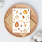 Postkarten-Set Herbstliebe 6 Karten A6: Aquarell-Kürbisse und Blätter auf einer Holzplatte, ideal für Grüße und Herbstdekoration, gedruckt auf hochwertigem Naturpapier.