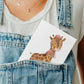 Karte Giraffe Vintage A6: Person hält Karte mit gezeichneter Giraffe im Hut im Overall-Tasche, passend als Gruß- oder Glückwunschkarte.