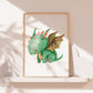 Poster Baby-Feuerdrache A3 & A4: grüner Drache auf einem weißen Untergrund. Ideal als Kinderzimmerdeko, gedruckt auf hochwertigem, mattem Naturpapier. Gerahmt auf Regal.