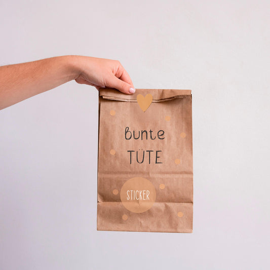 Hand hält eine braune Papiertüte mit schwarzen Text, die Bunte Tüte Sticker glossy und matt enthält, über 30 Sticker für Journal und Scrapbooking.