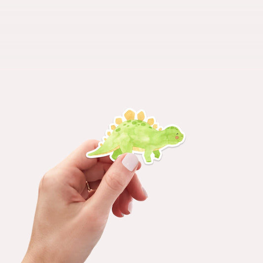 Sticker Dinosaurier Stego: Hand hält einen handgemalten Vinyl-Dino-Sticker. Ideal für Bullet Journals, Laptops oder Bastelprojekte. Spritzfest und langlebig.