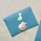 Sticker Dinosaurier hellgrün auf blauem Umschlag mit Muschel. Handgefertigter, spritzfester Vinyl-Sticker, ideal für Bullet Journals, Schulhefte und kreative Dekorationen.