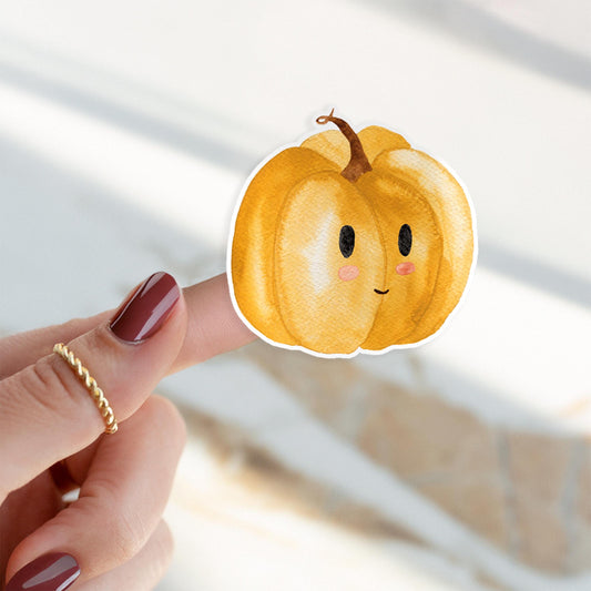 Ein Finger hält einen handgemalten Kürbis-Sticker aus hochwertigem Vinyl, ideal zur Dekoration von Notizbüchern und Geräten.