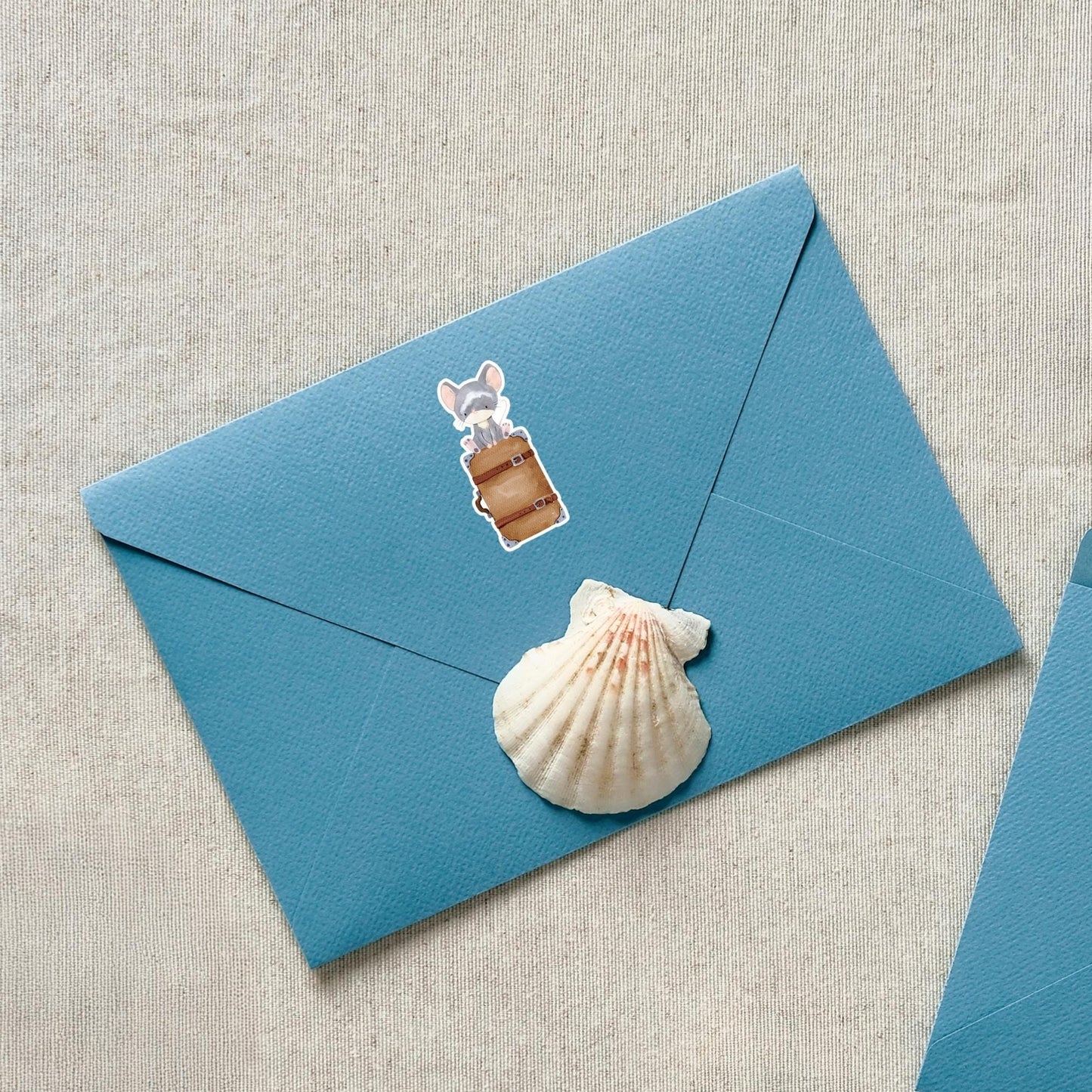 Sticker Maus & Koffer: Nahaufnahme eines blauen Umschlags mit Muschel und Cartoon-Maus auf Koffer, ideal für kreative Anwendungen und Dekoration.