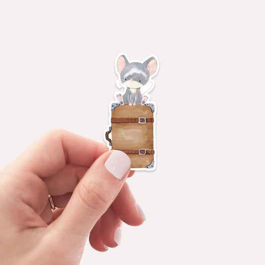 Eine Hand hält den Sticker Maus & Koffer, der eine Cartoon-Maus auf einem Koffer zeigt, ideal für Bullet Journals oder Laptops.