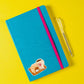 Sticker Frühstück: Ein blauer Notizblock mit rosa Band und Stift, inspiriert von Kaffee und Croissant, ideal zur Dekoration von Bullet Journals und Laptops.