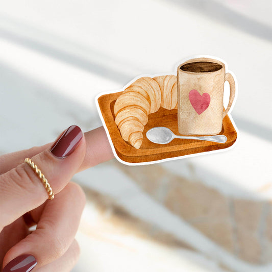 Sticker Frühstück: Ein Finger zeigt einen handgemalten Kaffee- und Croissant-Sticker. Hochwertiger Vinyl-Aufkleber, ideal für Bullet Journals oder Laptop-Dekoration.