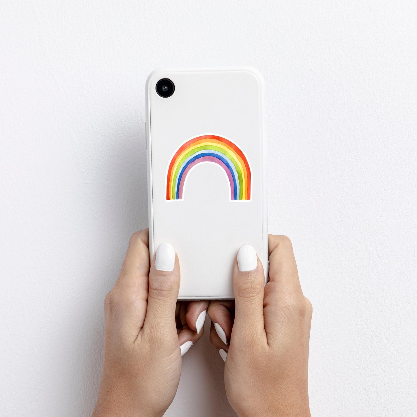 Hände halten ein kleines weißes Smartphone mit dem Sticker Regenbogen, einem handgemalten Vinyl-Aufkleber, der positive Energie ausstrahlt, spritzfest und langlebig.