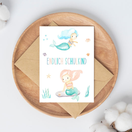 Karte Endlich Schulkind Meerjungfrau A6 zeigt zwei Meerjungfrauen und Fische auf einer pastellfarbenen Postkarte, perfekt für Einschulungsglückwünsche oder Einladungen.