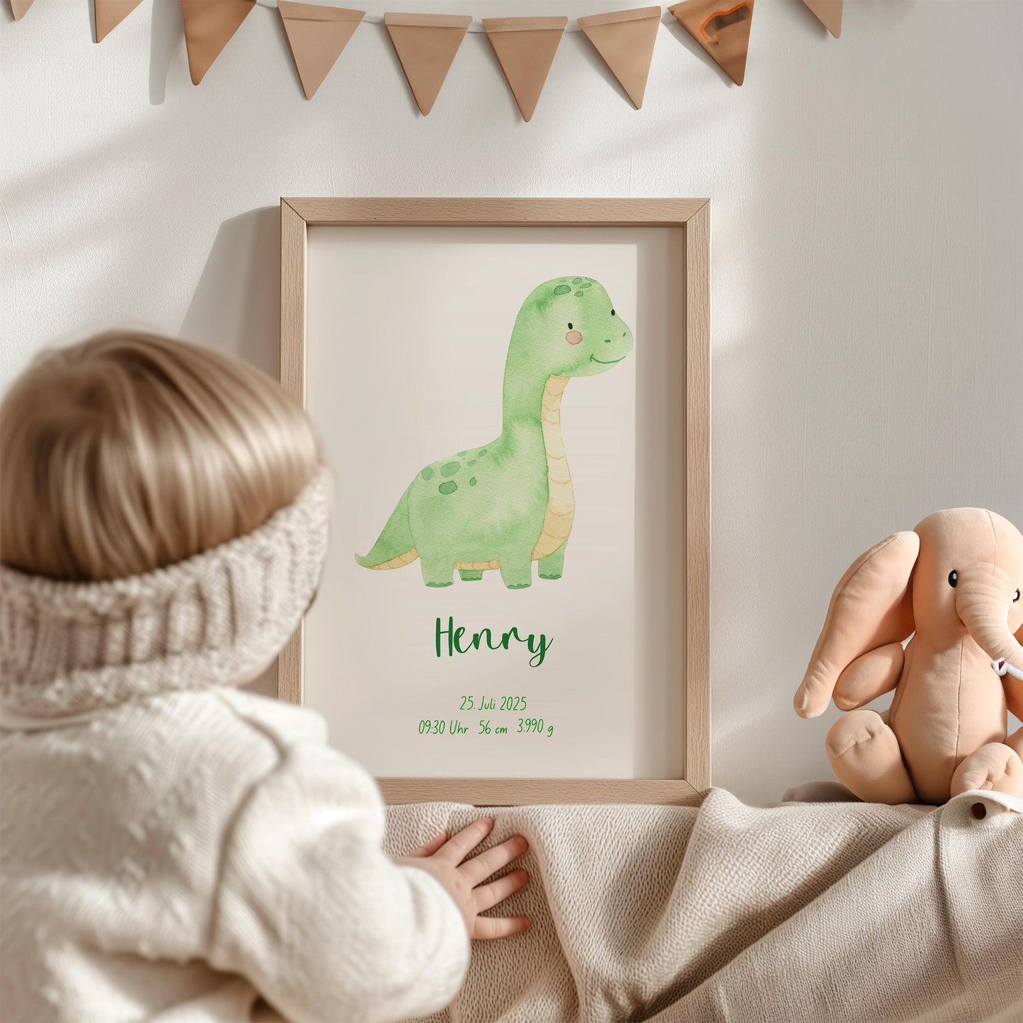 Kleinkind greift nach Geburtsposter Dino personalisiert, das einen grünen Dinosaurier und Geburtsdetails zeigt, neben einem Elefanten-Plüschtier und Wimpelgirlande im Kinderzimmer.