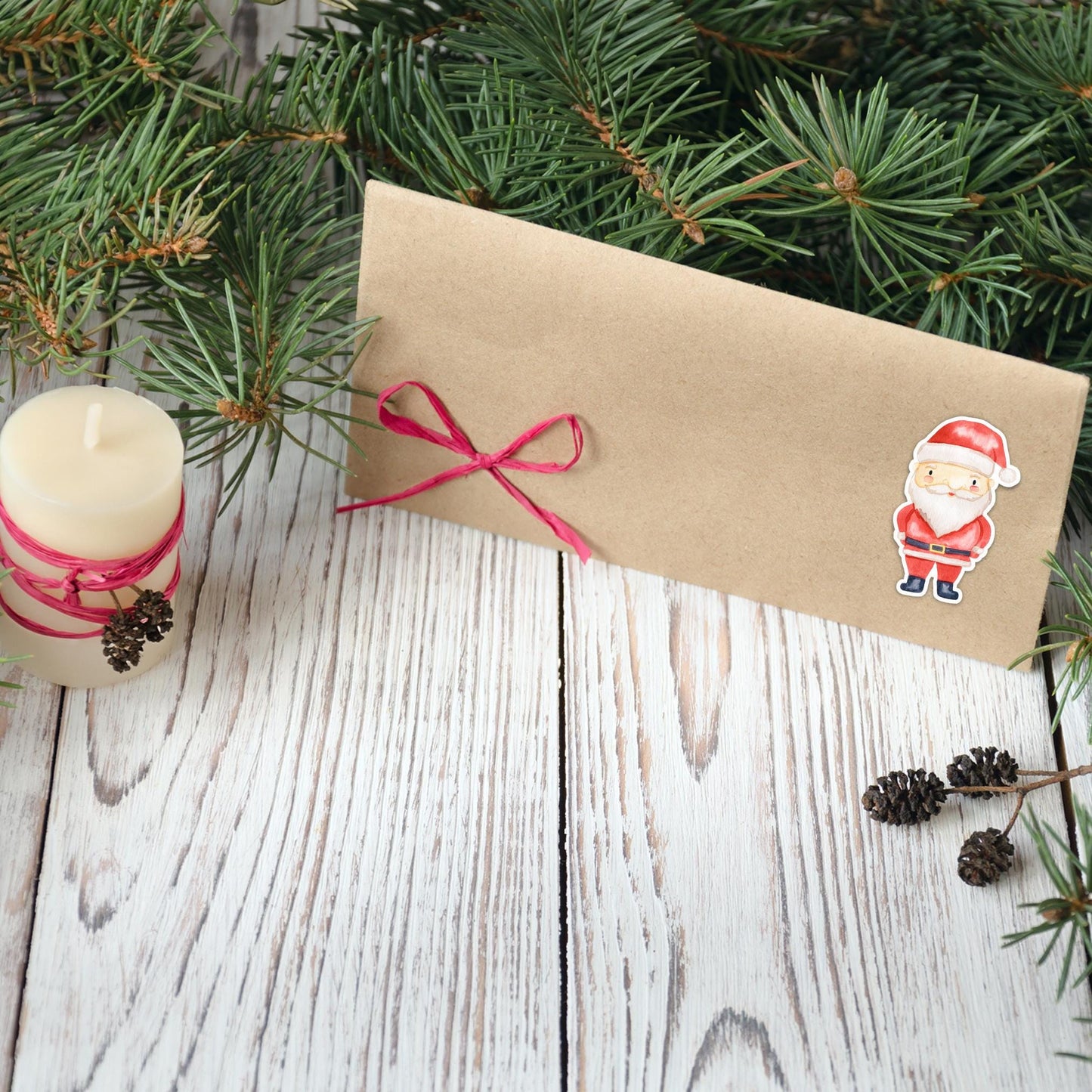 Sticker Weihnachtsmann auf einem kraftpapier Umschlag mit rotem Band, umgeben von Tannenzweigen, Kerze und Tannenzapfen – ideal für Weihnachtskarten und Dekoration.