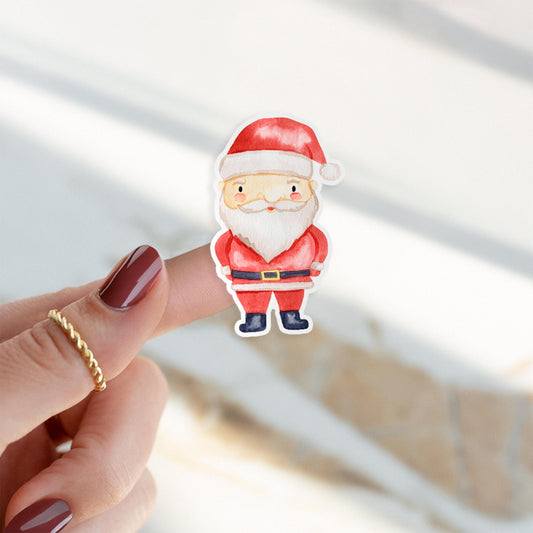 Sticker Weihnachtsmann: Handgezeichnete, ausgeschnittene Vinylfigur, cartoonartiger Weihnachtsmann in rotem Anzug, gehalten von Hand mit burgunderroten Nägeln und goldener Ring.