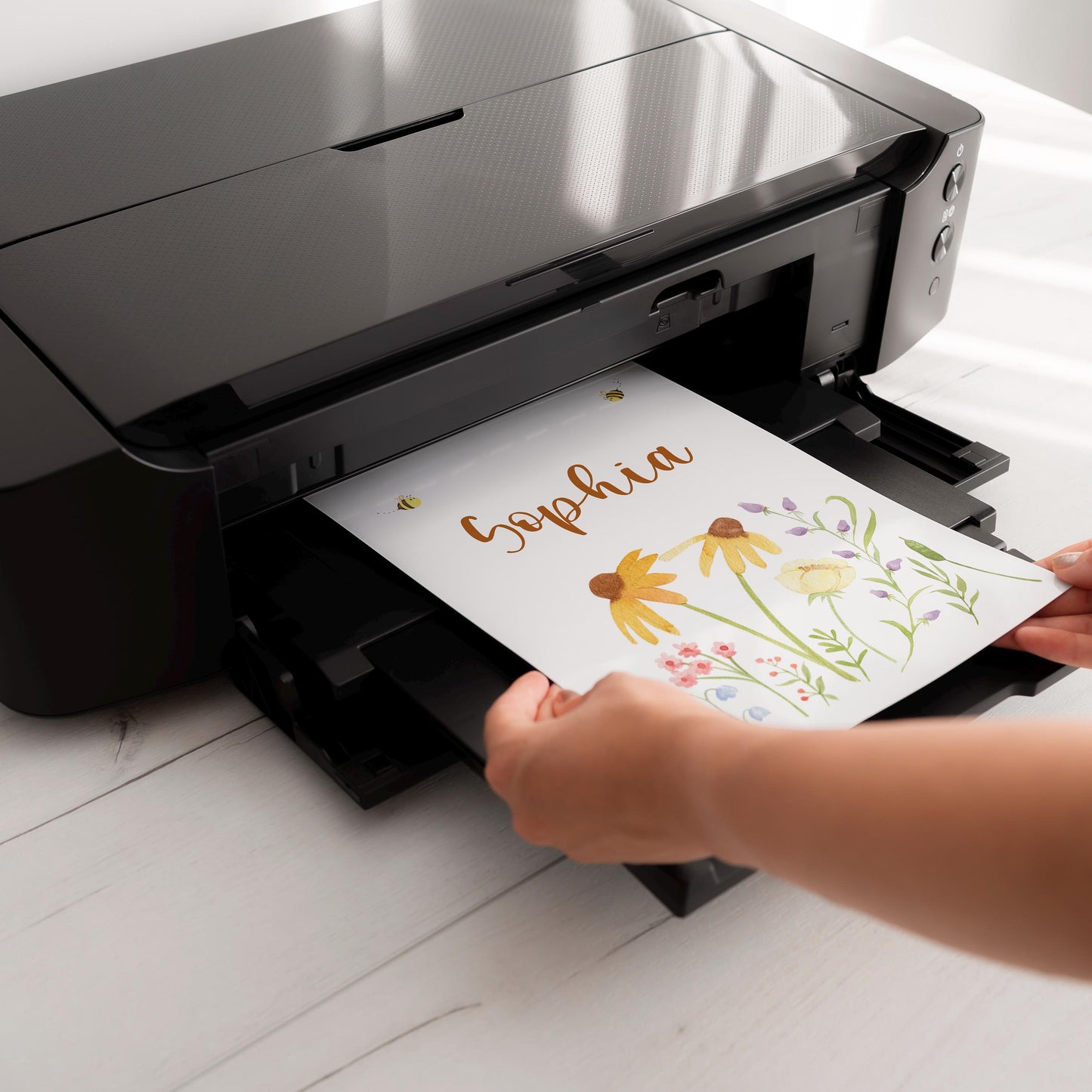 Ein schwarzer Tintenstrahldrucker druckt ein personalisiertes Namensposter aus dem 3er Set Bären und Bienen, mit Aquarell-Blumendesign und dem Namen Sophia.