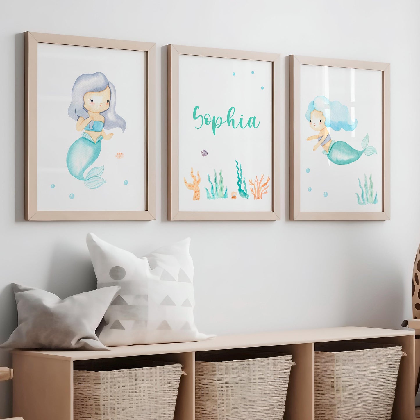 Namensposter personalisiert im 3er Set: Meerjungfrau. Zwei Meerjungfrauen-Illustrationen und personalisiertes Namensposter, dekorativ über einer Bank mit Kissen und Körben platziert.