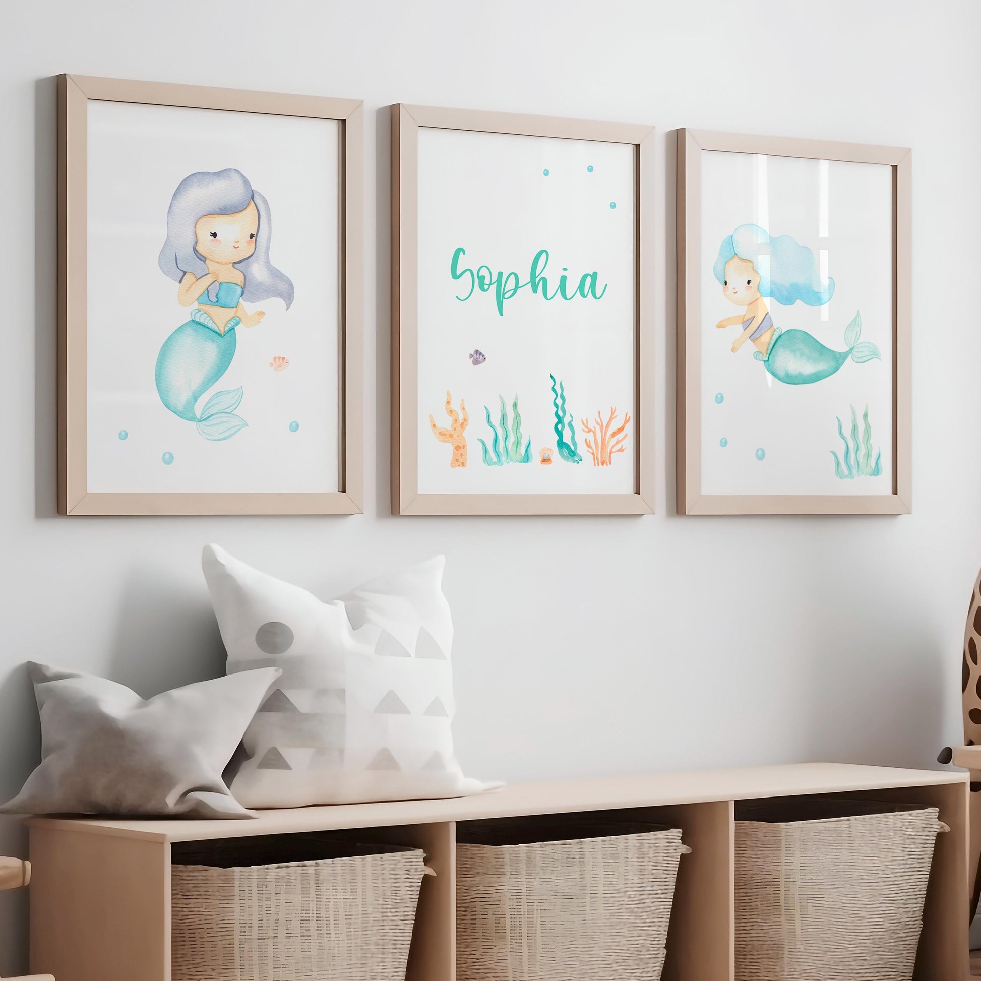 Namensposter personalisiert im 3er Set: Meerjungfrau. Zwei Meerjungfrauen-Illustrationen und personalisiertes Namensposter, dekorativ über einer Bank mit Kissen und Körben platziert.