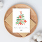 Personalisierte Weihnachtskarte Weihnachtsbaum A6 auf Holztablett mit Aquarell-Tannenzweig, Poinsettien und Frohe Weihnachten Sophie-Schriftzug. Umgeben von Baumwollzweigen, inkl. Umschlagoption.