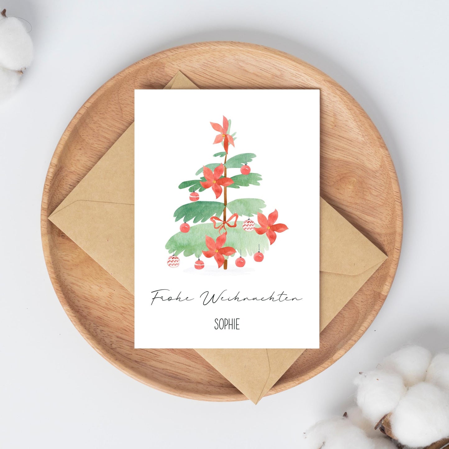 Personalisierte Weihnachtskarte Weihnachtsbaum A6 auf Holztablett mit Aquarell-Tannenzweig, Poinsettien und Frohe Weihnachten Sophie-Schriftzug. Umgeben von Baumwollzweigen, inkl. Umschlagoption.