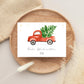 Personalisierte Weihnachtskarte Auto & Baum A6 auf Holzteller, mit vintage rotem Pickup und Weihnachtsbaum, umgeben von natürlichen Elementen, wie Gräsern und Stoff.